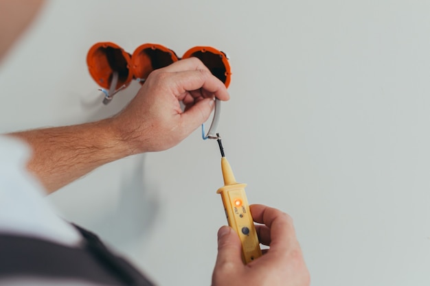 Male worker professional electrician mounts an electrical outlet in the apartment after repair, close-up photo of the installer