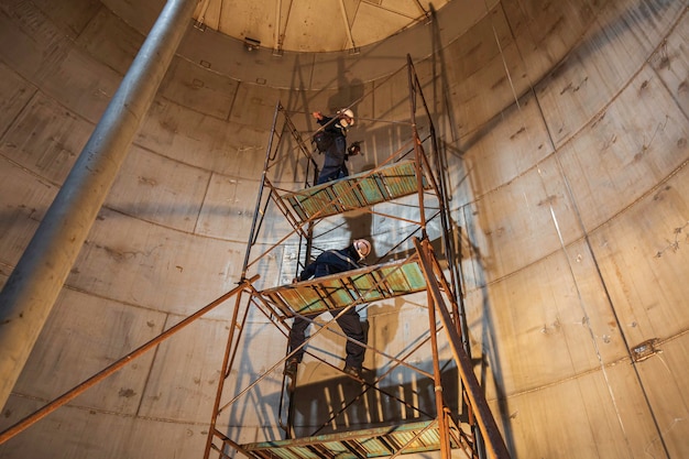 Male worker in progress tank stainless oil inspection scaffolding in confined space