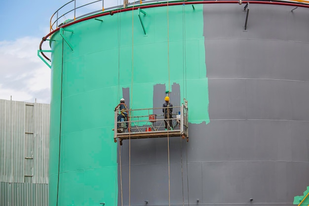 The male worker takes the cable car holding an industrial painting brush used for shell plate tank oil surface surface green color