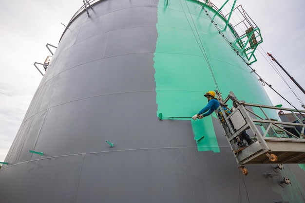 The male worker takes the cable car holding an industrial painting brush used for shell plate tank oil surface surface green color