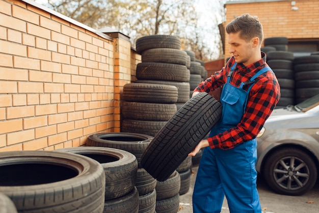 Photo male worker in uniform at the stack of tyres, tire service.