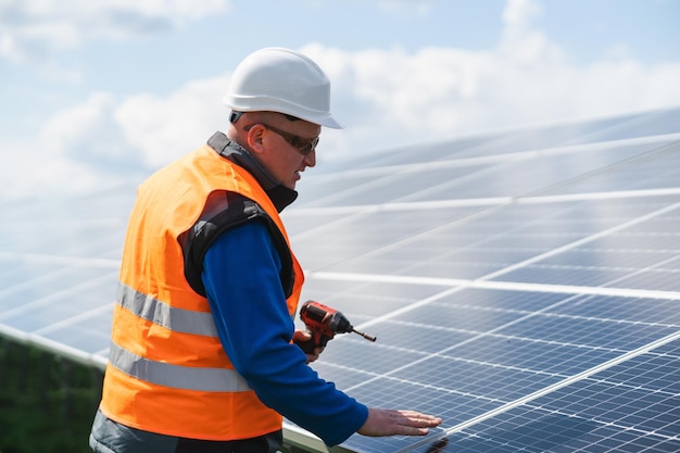 Male worker in uniform with drill  screwdriver in his hand on stepladder near solar panels