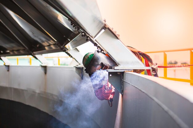 Male worker wearing protective clothing and beam roof repair welding industrial construction oil and gas or storage tank inside confined spaces.