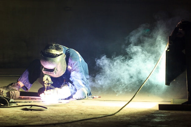 Male  worker wearing protective clothing repair  bottom plate storage tank industrial construction smoke spotlight inside confined spaces.