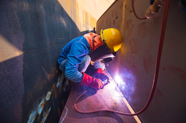 Male worker wearing protective clothing and repair welding industrial construction oil and gas or storage tank inside confined spaces.