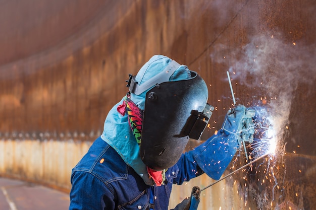 Male  worker wearing protective clothing and repair welding spark shell plate industrial construction oil and gas or  storage tank inside confined spaces.