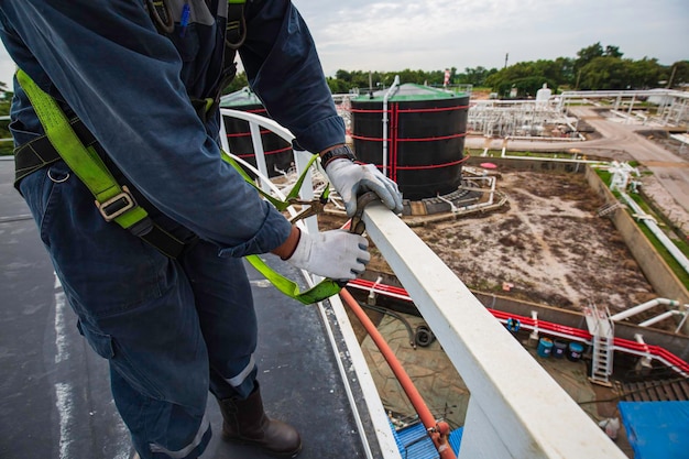 Male worker wearing safety first harness and safety lone working at high handrail place on open top tank roof oil