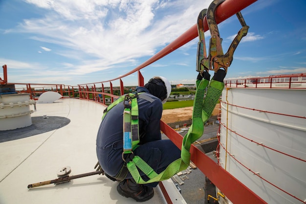 Male worker wearing safety first harness and safety lone working at high handrail place on open top tank roof oil