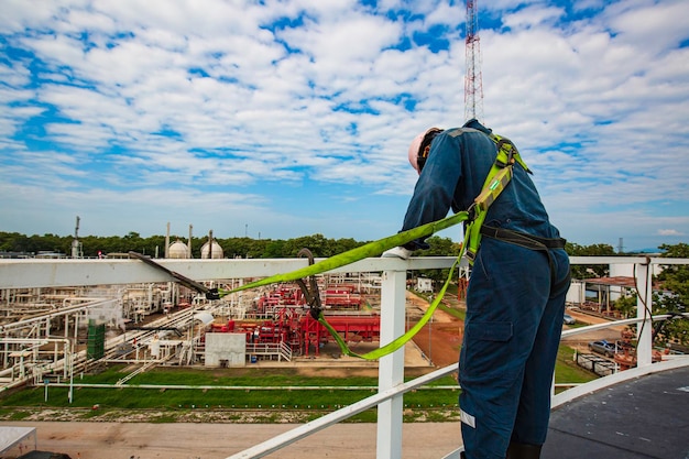 Male worker wearing safety first harness and safety lone working at high handrail place on open top tank roof oil