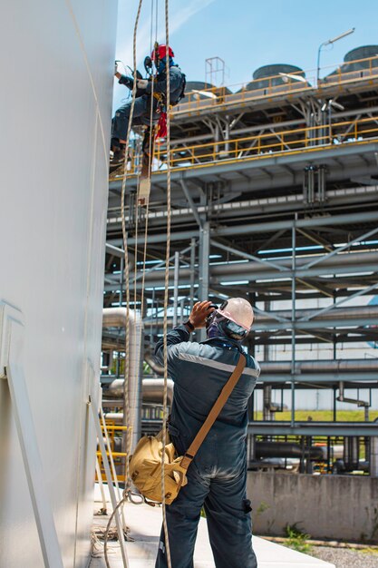 Male workers control rope down height tank rope access inspection of thickness shell plate storage tank safety work at height.