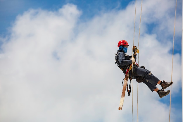 Male workers control swing rope down height tank rope access inspection of thickness shell plate tank gas background blue sky.