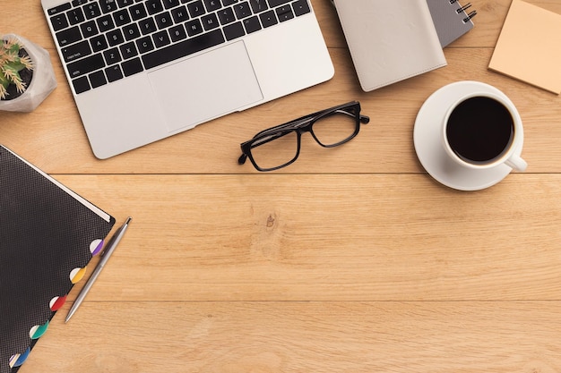 Male workplace with laptop, coffee cup, notebook and glasses. Wooden background, top view, mockup, copy space.