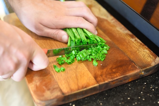 males hands cutting green onion on wooden board for cooking japanese ramen