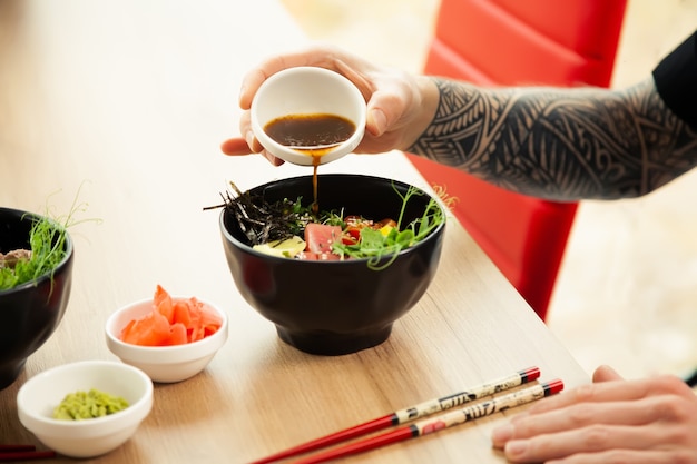 A man adds soy sauce to poke salad a mans hand pours soy sauce into a bowl of salad guy young man dr...