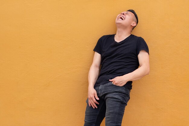 Man against yellow wall Laughing latin man in black shirt Natural laughter and guffaw