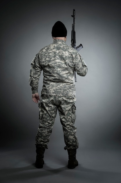 A man in an American camouflage uniform and a black sniper cap with a raised submachine gun. Military conflicts and danger. Full height. Gray background. Vertical.