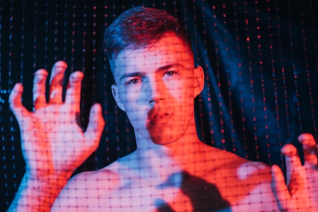 Man anxiety Self isolation loneliness Freedom security Art portrait of disturbed worried shirtless male hostage trapped behind cell in red blue neon light on dark background