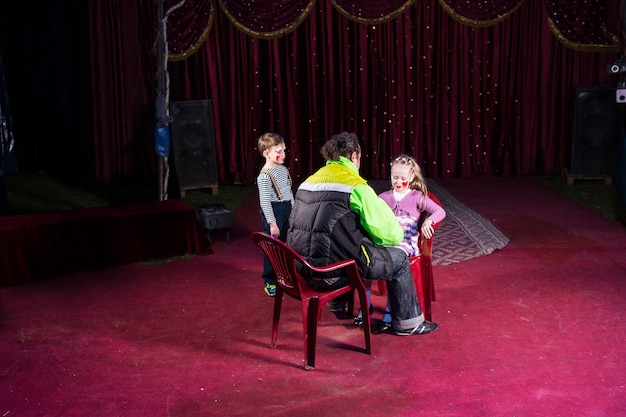 Man Applying Make Up to Faces of Young Boy and Girl on Empty Stage