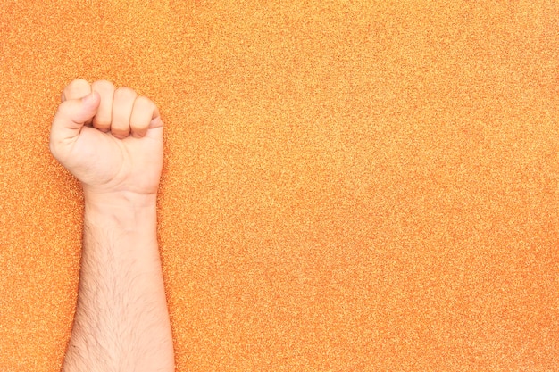 Man arm with clenched fist up from freedom fight on glitter orange background