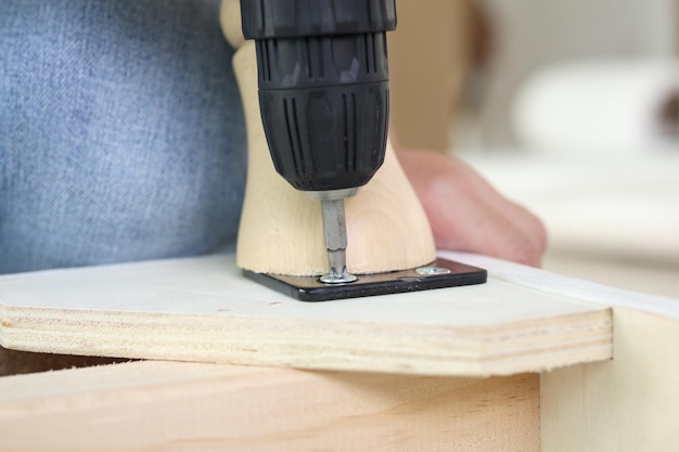 Man assembling sofa furniture at home using cordless screwdriver