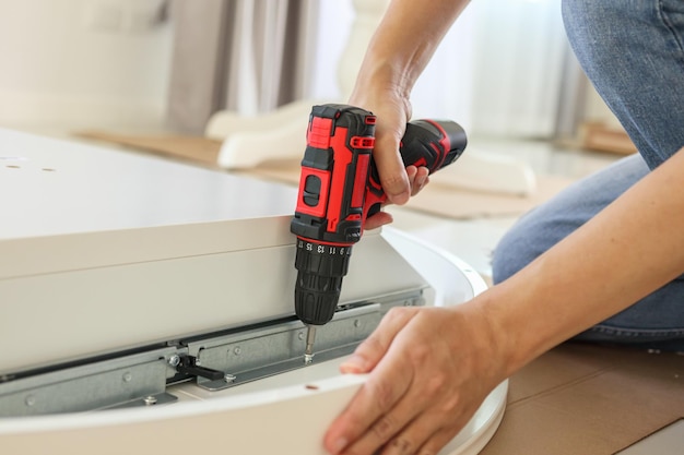 Man assembling white table furniture at home using cordless screwdriver