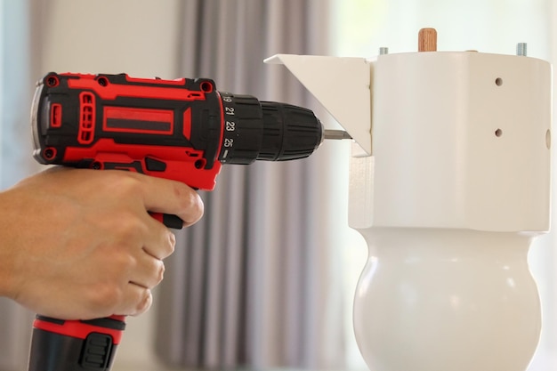 Man assembling white table furniture at home using cordless screwdriver