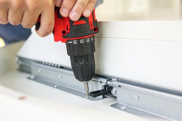 Man assembling white table furniture at home using cordless screwdriver