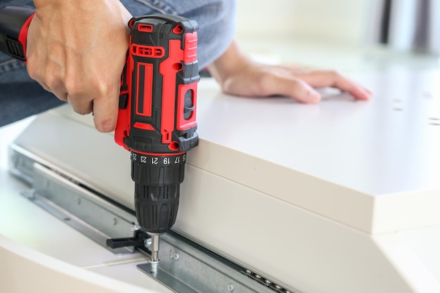 Man assembling white table furniture at home using cordless screwdriver