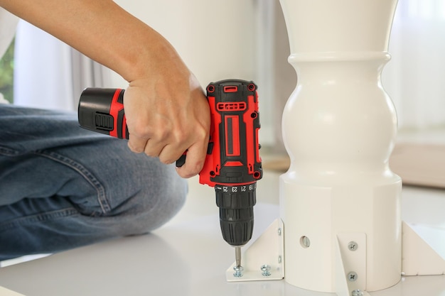 Man assembling white table furniture at home using cordless screwdriver