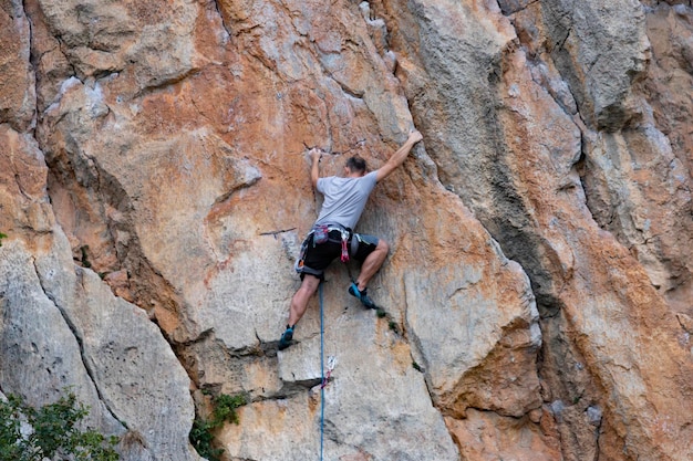 A man an athlete a rock climber on a sheer red rock The concept of active extreme recreation and hobbies View from the back