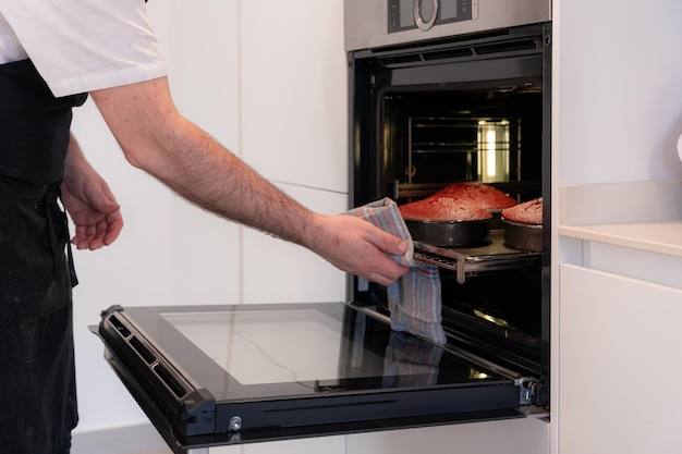 A man baker cooking a red velvet cake at home taking the baked cake out of the oven pans