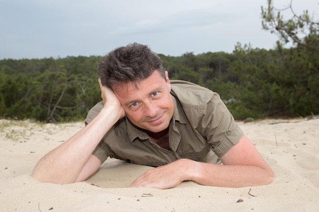 Man on beach lying in sand looking to side smiling happy