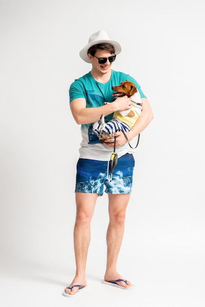 A man in a beach suit and flip flops with a Jack Russell Terrier in his arms