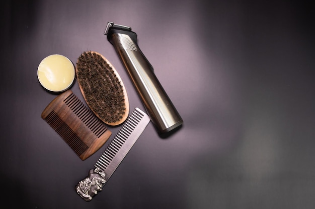 Man beard grooming items on a black background, wooden comb, oil, brush and electric trimmer.