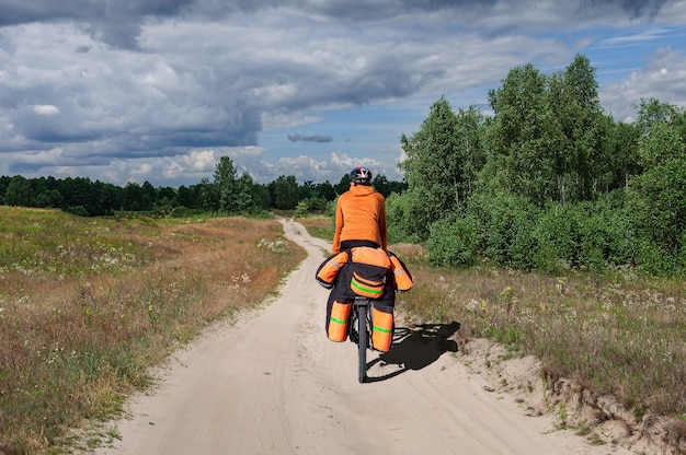 A man in a bicycle uniform with a large bicycle backpack rides a mountain bike on a dirt road