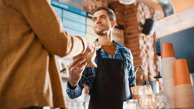 Photo a man in a black apron is handing a cup of coffee to a customer.