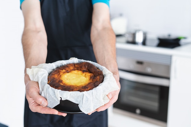 Man in black apron showing a cheesecake. Kitchen concept.