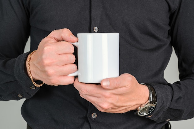 A man in black clothes holds a large white coffee mug in his hand, close-up