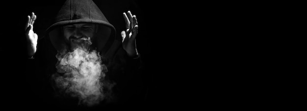 Man in a black hood and smoke on a black background