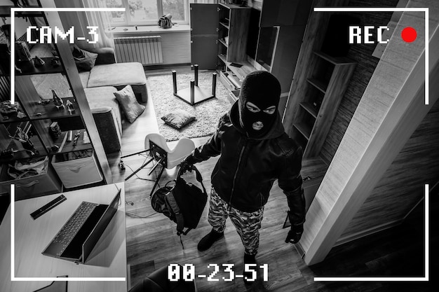 A man in a black mask is trying to rob a house There is recording on an outdoor video surveillance camera Robbery of a private house Criminal concept black and white camera recording effect