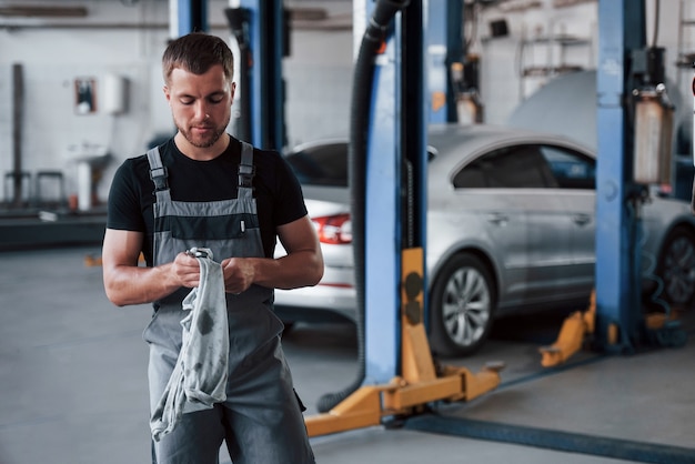 Man in black shirt and grey uniform stands in garage after repairing broken car