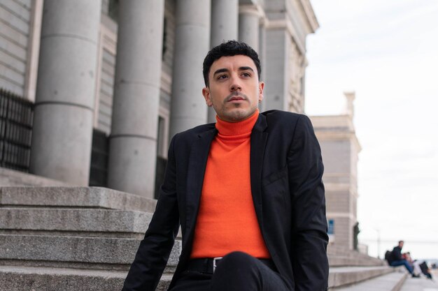 A man in a black suit sits on a stone steps in front of a building.