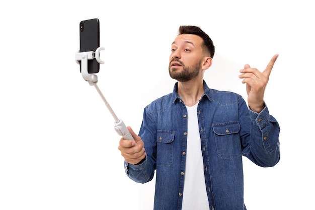 A man in a blue denim shirt is broadcasting a video while holding a smartphone on a selfie stick