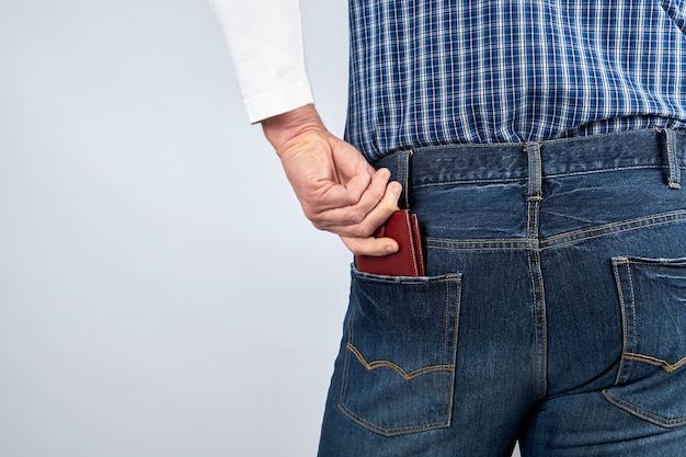 Man in blue jeans and a plaid shirt shoves a leather brown wallet in the back pocket 