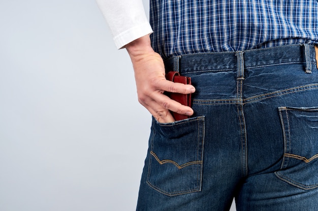 Man in a blue plaid shirt and jeans puts a leather wallet in his back pocket