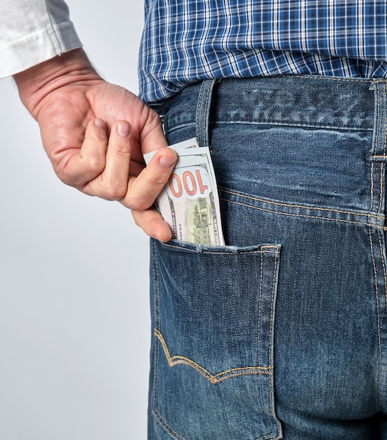 Man in a blue plaid shirt and jeans puts paper American dollars in his back pocket