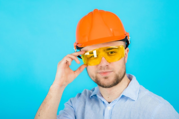 man in a blue shirt in a protective orange helmet and a white notebook stands on a blue background