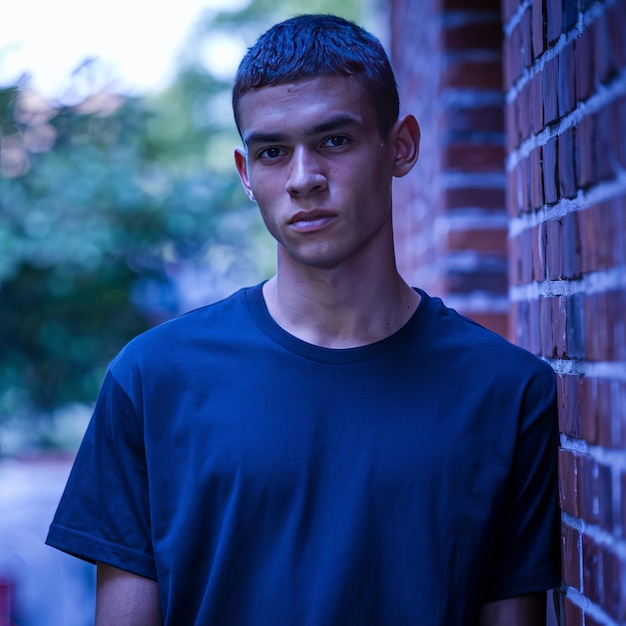 a man in a blue shirt stands in front of a brick wall