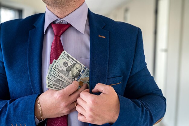 Man in blue suit and red tie putting bribe dollar bills into his pocket corruption concept