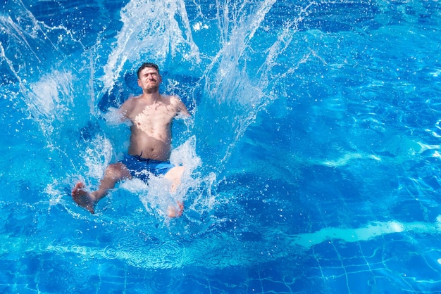 Man in blue trunks jumping in the pool with splashes